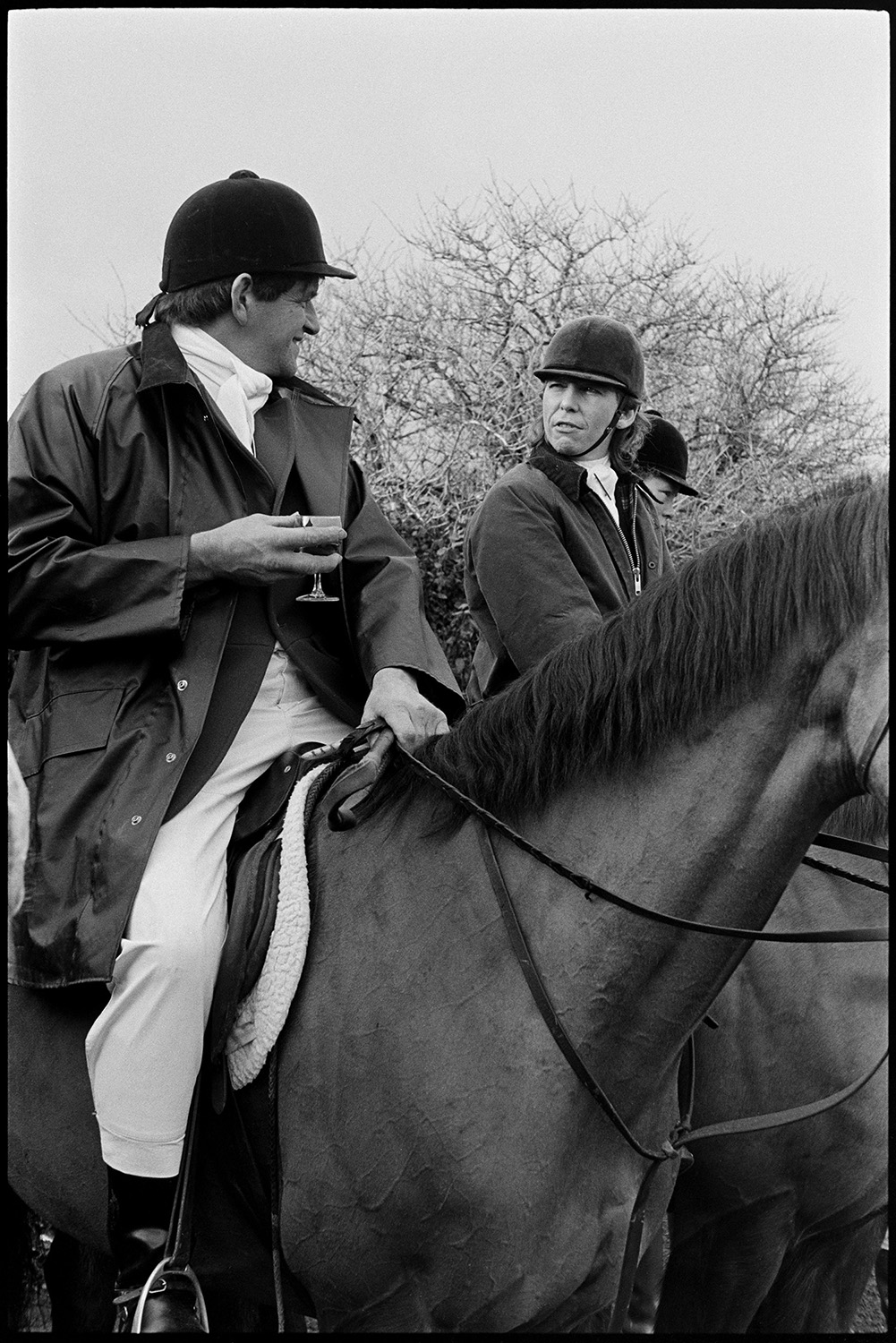 Hunt meet in village, setting off, horses and riders waiting in rain on lonely road. 
[A huntsman on horseback drinking a stirrup cup at a hunt meet in Petrockstowe.]