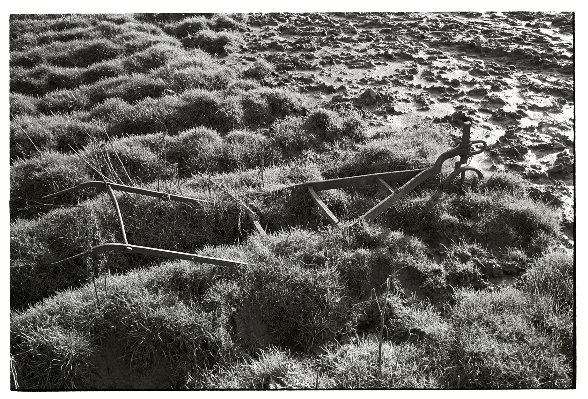Old rusty abandoned plough  in muddy field.
[An abandoned old hand plough half buried in a muddy field at Mousehole, Upcott.]