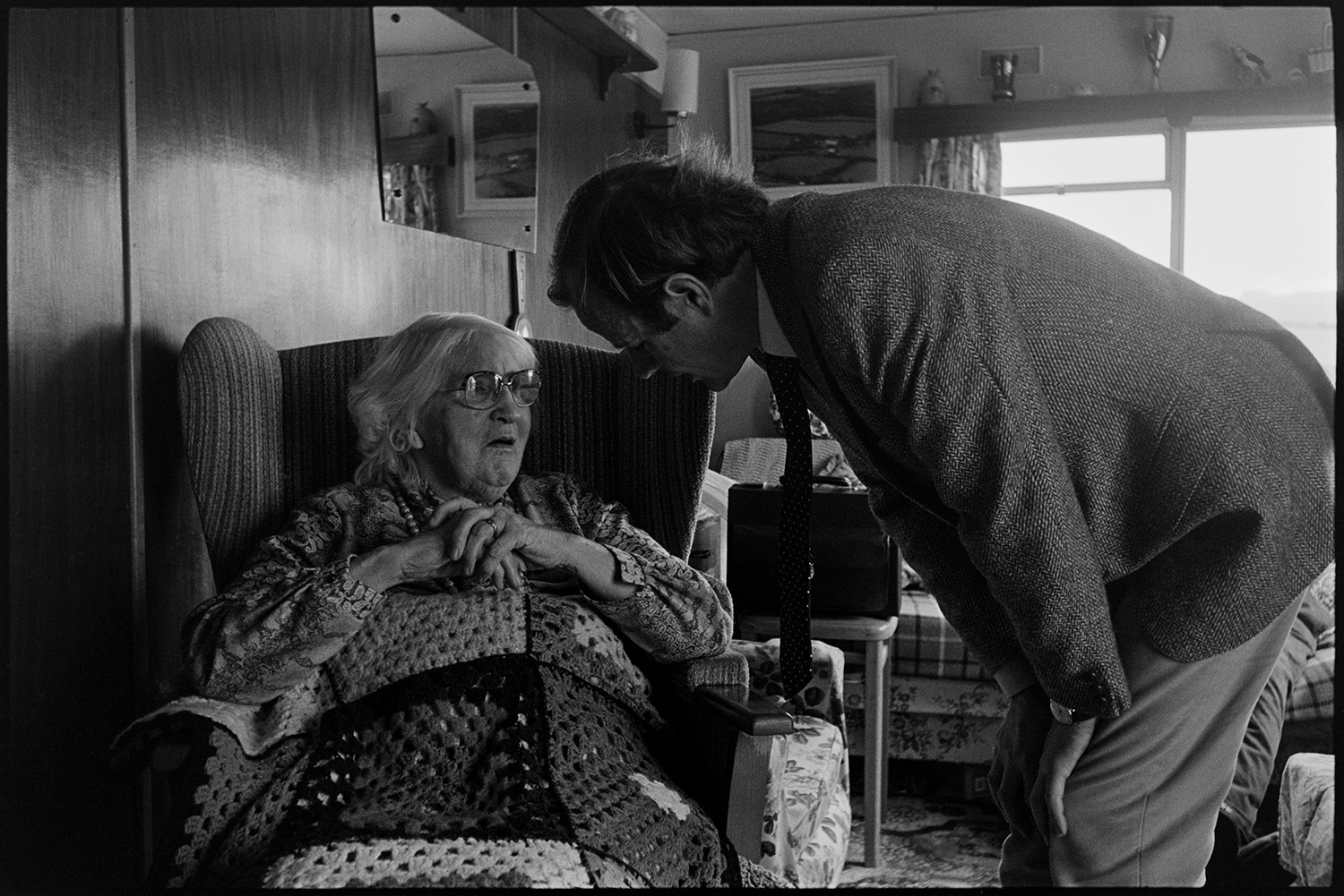 Doctor on his rounds talking to man about his wife, doctor chatting with his wife. 
[Doctor Richard Westcott visiting a patient in her home, possibly at Mariansleigh. She is sat in an armchair with a blanket over her. A mirror is hung on the wall in the background.]
