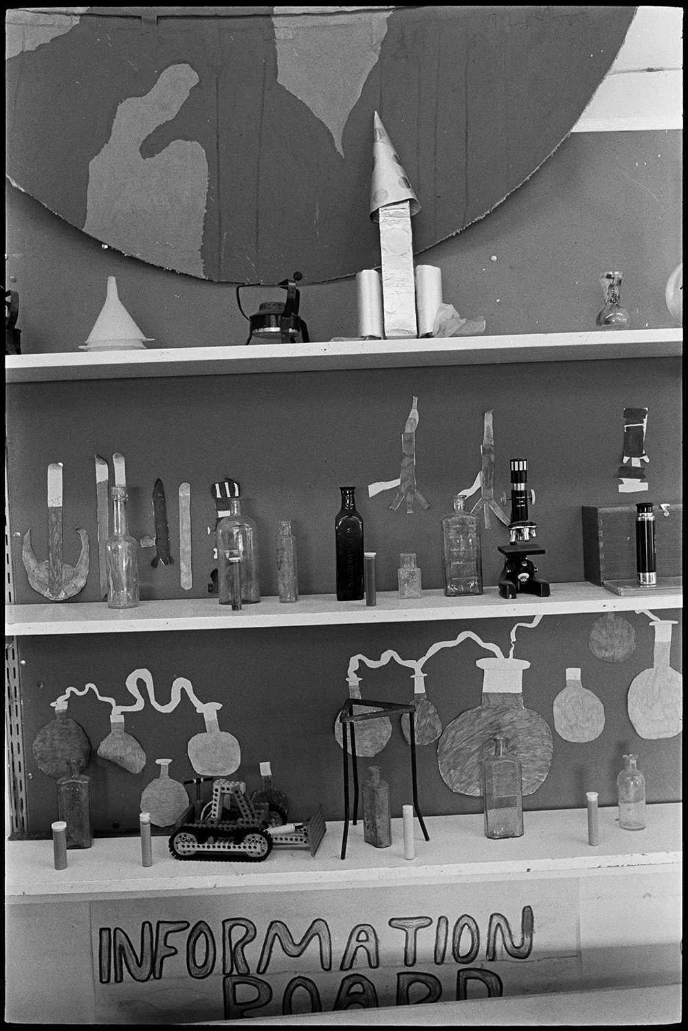 Schoolchildren working on space project pretending to be astronauts in spacecraft. 
[A display of children's school work in a classroom in Bideford Primary School about a space project they have been working on. The display includes bottles, a Bunsen burner, microscope, pictures of test tubes and a model digger.]