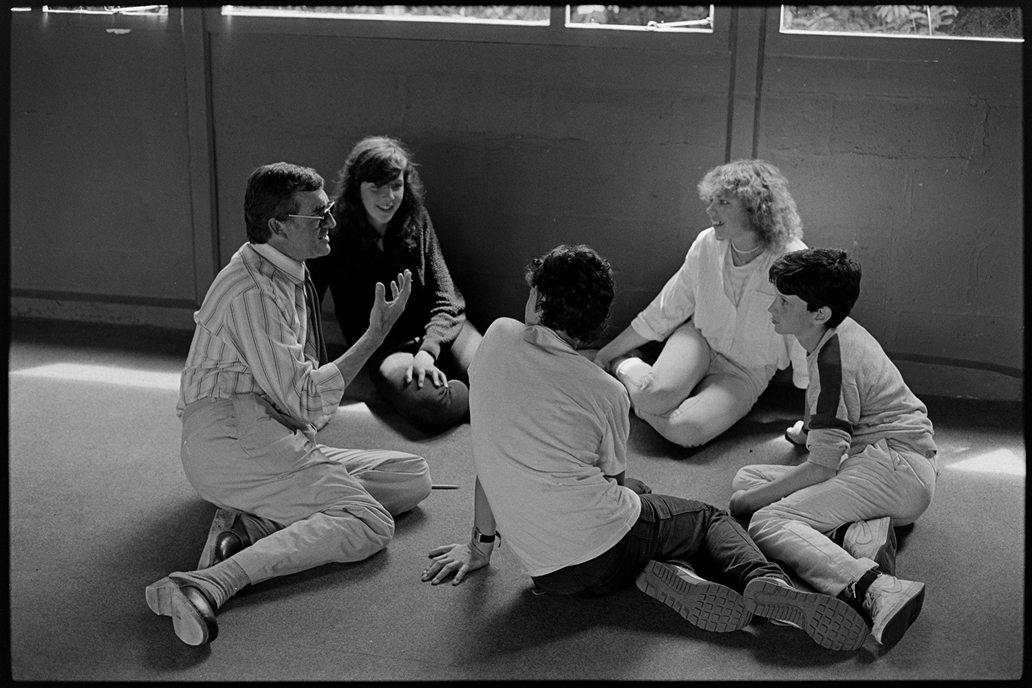 Music class in school, visiting teacher with staff and pupils playing music and advising. 
[Four pupils sat on the floor talking to a teacher in a drama lesson at Holsworthy School.]
