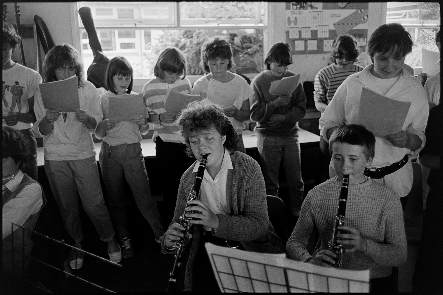 Music class in school, visiting teacher with staff and pupils playing music and advising. 
[Pupils singing and playing clarinets in a music lesson at Holsworthy School.]