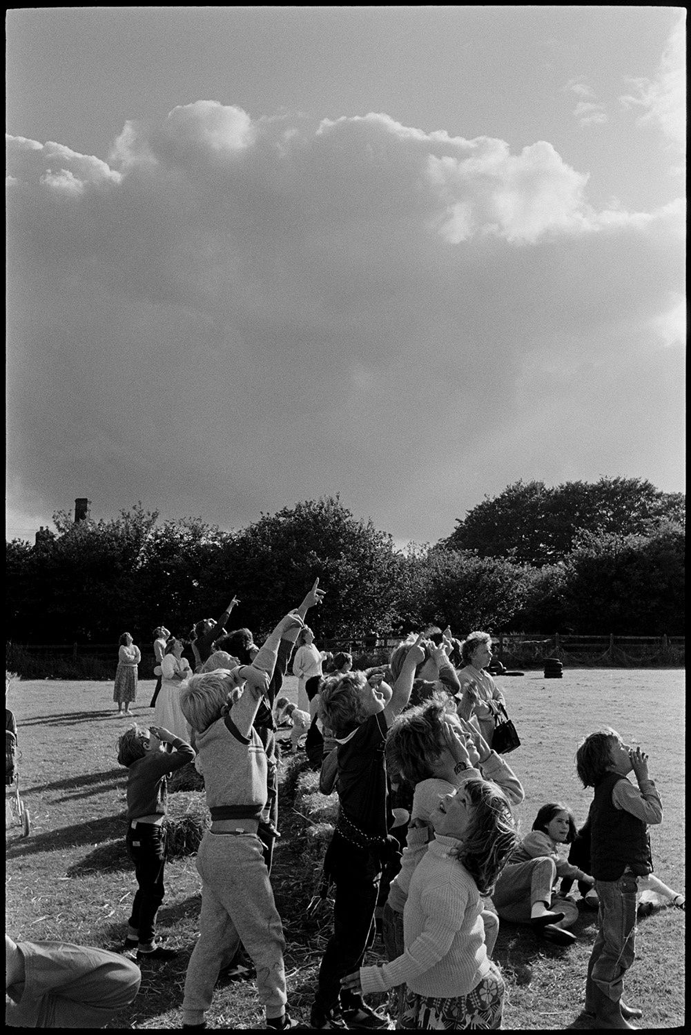 Sports Day, parachute landing races and spectators. 
[Children pointing up to the sky at two parachutists at Dolton School sports day.]