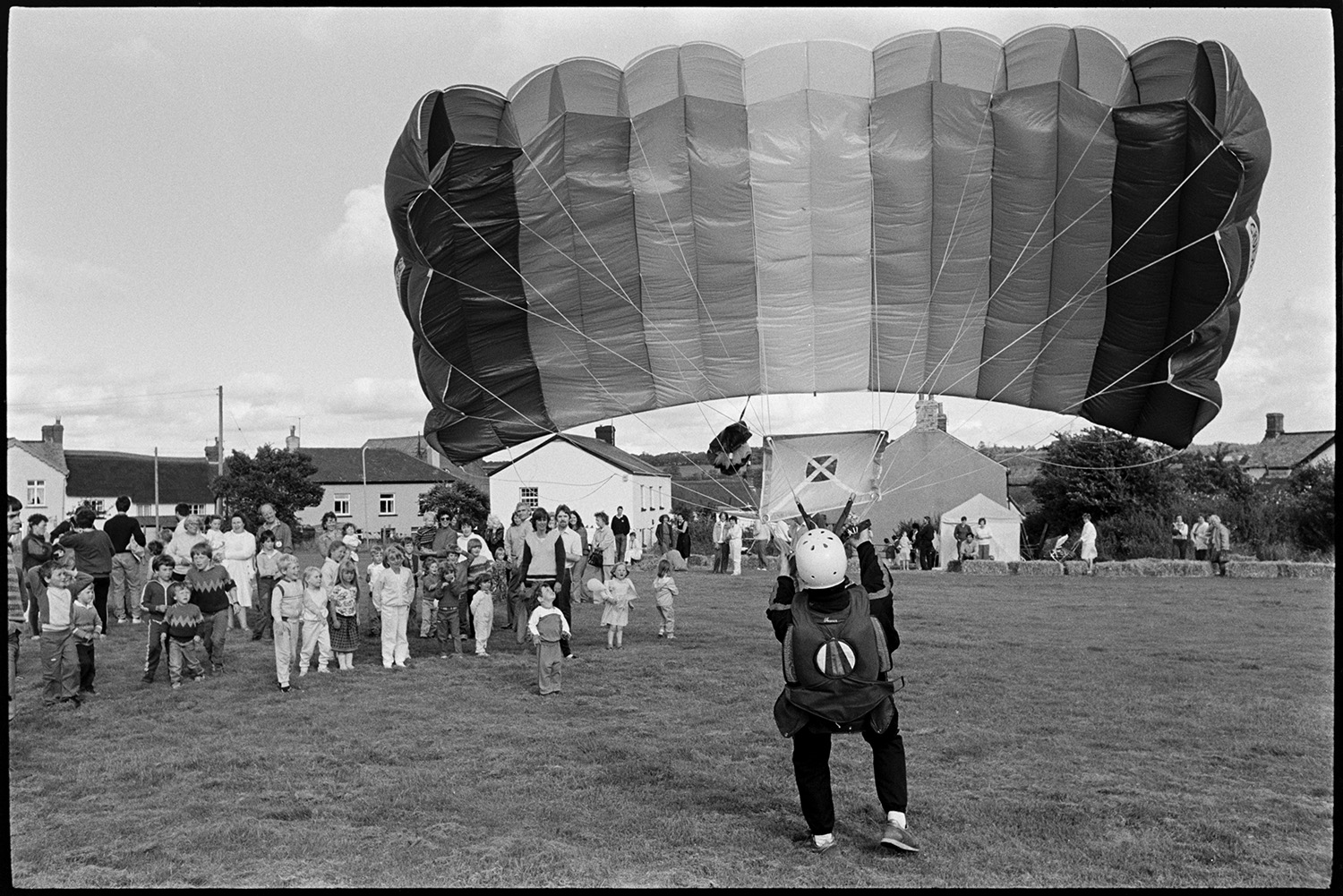 Sports Day, parachute landing races and spectators. 
[A parachutists who has just landed at Dolton School sports day, demonstrating their parachute for the children and adults at the sports day.]