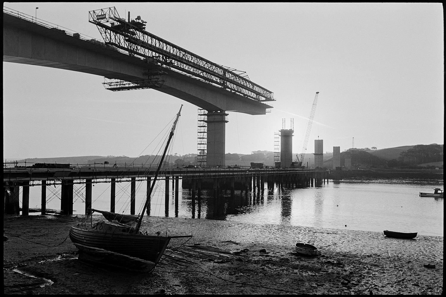 Construction of new bridge across river. 
[Cranes constructing Bideford New Bridge across the River Torridge. Boats can be seen on the mud flats of the river.]