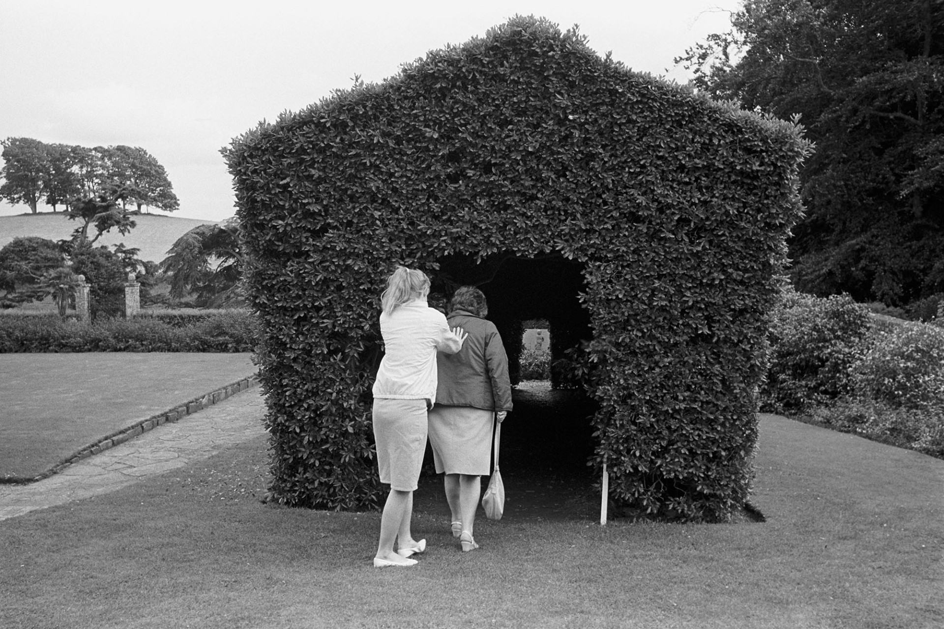 Tree house in park of stately home, girl pushing woman into tunnel cut through centre. 
[A girl and woman at Tapely Park stately home and garden at Instow. The girl is pushing the woman into a tree house in the park or garden.]