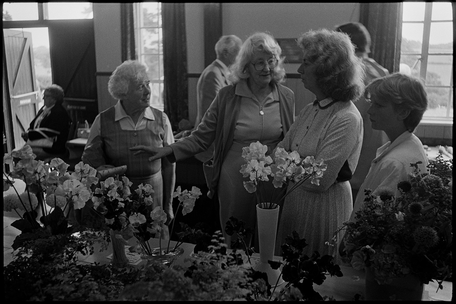 Flower show exhibits, village hall, flowers, jam, vegetables, prize winner with cup.
[Women looking at floral displays and exhibits at the Flower Show in Dolton Village Hall.]