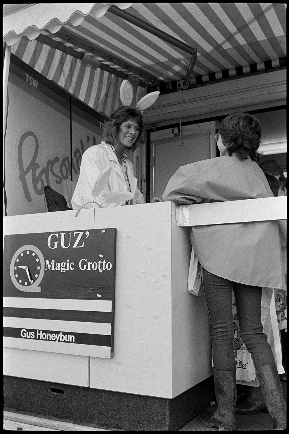 Agricultural show, prize sheep, exhibition, TV tent.
[Entrance to the Gus Honeybun tent at the North Devon Show in Alverdiscott. A television presenter wearing rabbit ears is talking to a visitor. Signs for TSW and Magic Grotto are at the tent entrance.]
