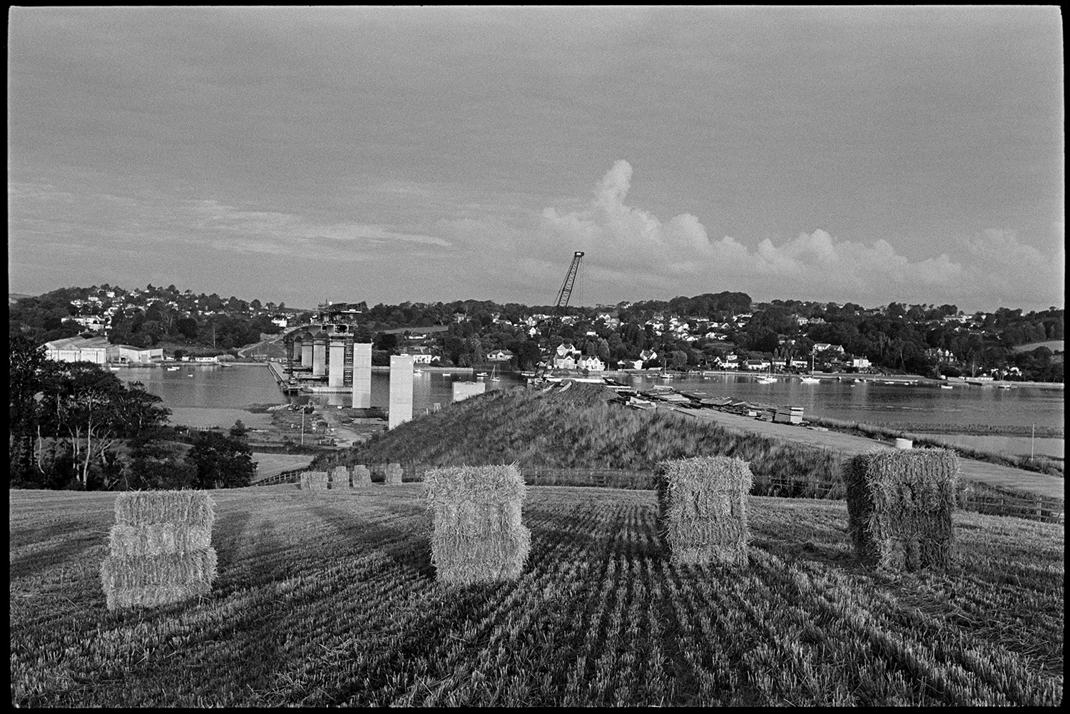 Bales of hay with bridge under construction in background.
[Straw bales standing in a field at Bideford with Bideford New Bridge being built over the River Torridge in the background.]