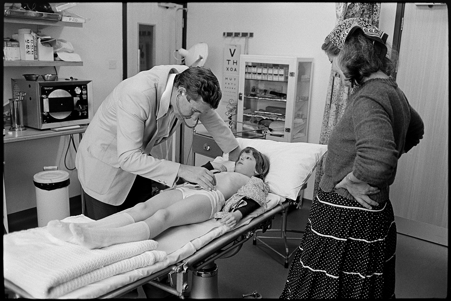 Doctor examining young girl at health centre.
[Dr Lamb examining a girl at Torrington Health  Centre, with her mother looking on.]