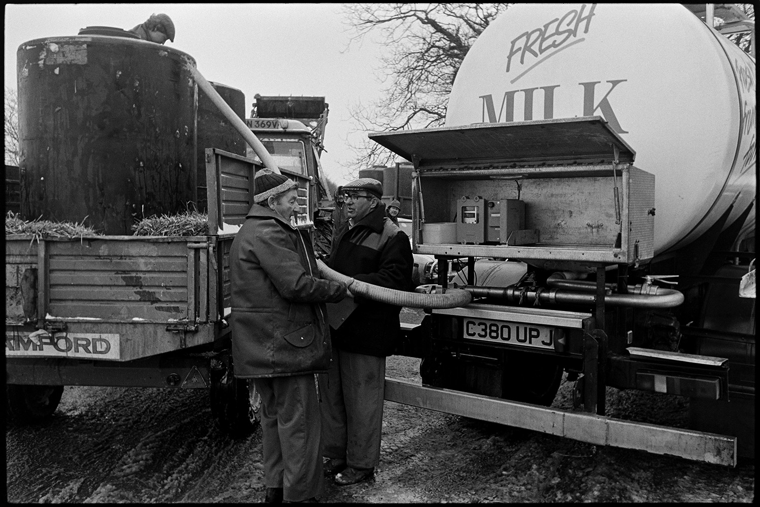 Snow, loading milk tanker, which could not get down snowbound farm lanes.
[Three men siphoning milk from tanks in a trailer into a milk tanker in a lane at Dolton Beacon, when the tanker could not get to the farms because of snowbound and icy lanes.]