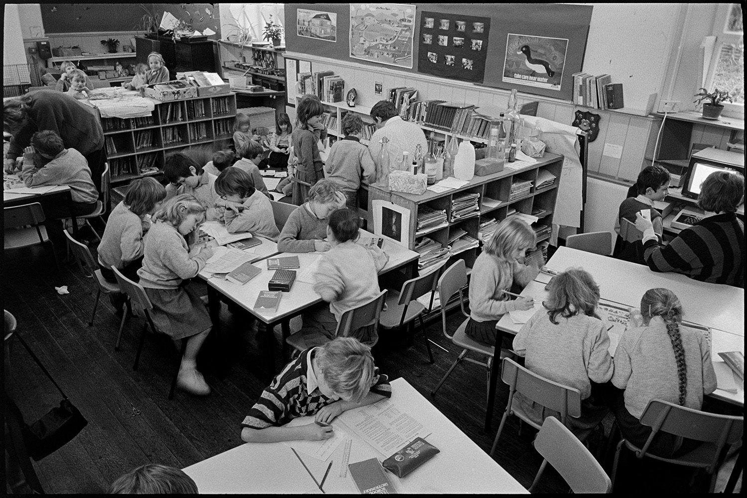 Interior of primary school with children at work, to show crowding to get new building.
[Interior of Dolton Primary School showing a classroom with children working at tables and in front of a computer in between books shelves. Three teachers are also in the classroom. The image was taken to demonstrate overcrowding in the school.]
