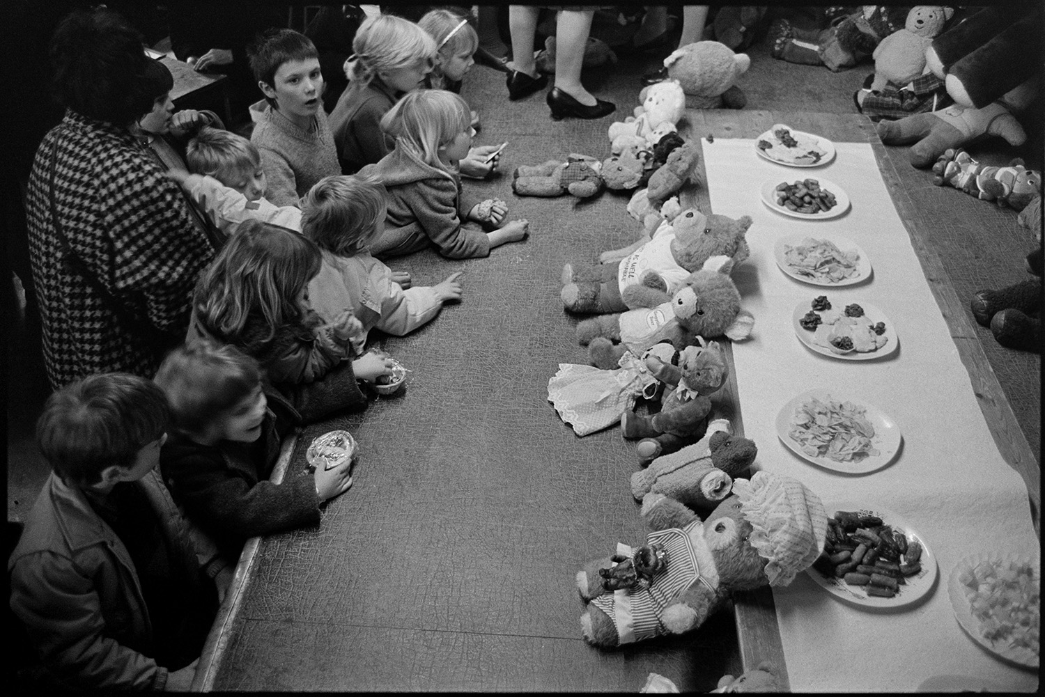 Easter show in village hall teddy bears party, cometition for the oldest bear.
[A group of children looking at a display of teddy bears arranged in a Teddy Bears Picnic tableau in the Easter Show at Dolton Village Hall. Biscuits and crisps are laid out for the teddy bears.]