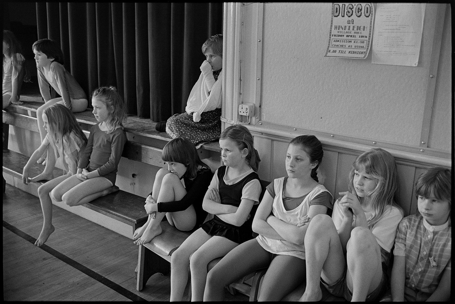 Dance class, children dancing performance in front of parents.
[A group of girls sitting on the stage and bench seats in Winkleigh Village Hall, attending Sally Barber's dance class and watching a performance in front of parents. A notice can be seen behind the children advertising a Disco in the village hall.]