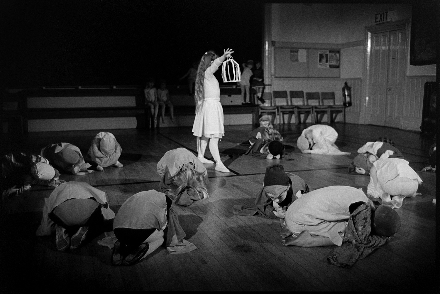 Dance class, children dancing performance in front of parents.
[Children in Sally Barber's dance class performing a dance in front of parents and family in Winkleigh Village Hall. One girl is holding a lantern.]