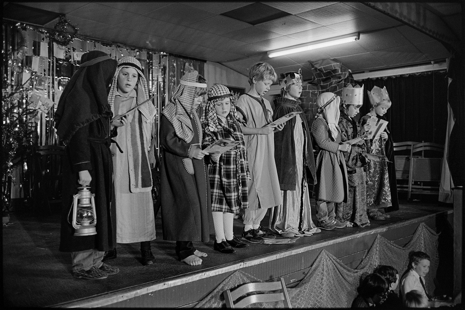 Christmas show in village hall Nativity play, children performing.
[Children singing in a Christmas show on the stage in Dolton Village Hall, dressed as shepherds and kings in the nativity story.]