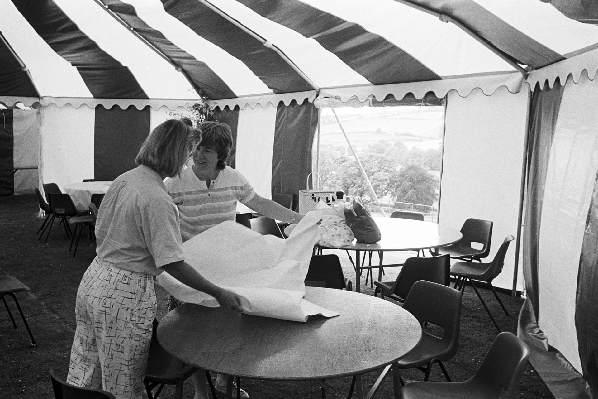 Women decorating marquee tent for hunt ball, preparing tables chatting. 
[Mrs Martin, on the left, and another woman decorating tables in a marquee at Colleton Manor, Chulmleigh, for a hunt ball.]