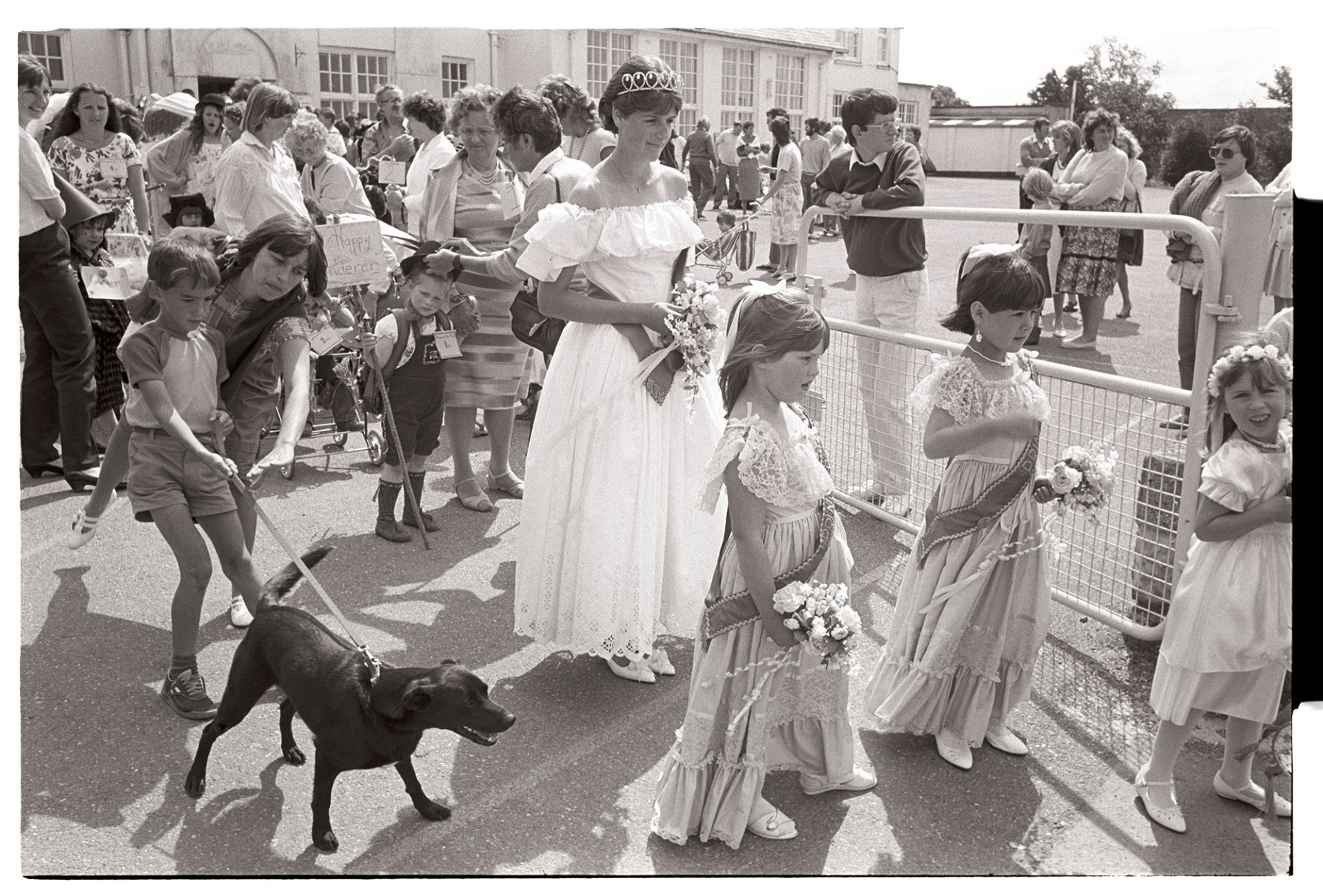 Procession, Queen and attendants about to set off to parade into village. Boy and dog too! 
[Debbie Hawkins, Chulmleigh Fair Queen, and her attendants setting off to parade through the town for the Fair. They are holding bouquets of flowers. A woman is about to hold back a boy and dog who are joining the parade. Other people, including children in fancy dress, are getting ready for the parade in the background.]