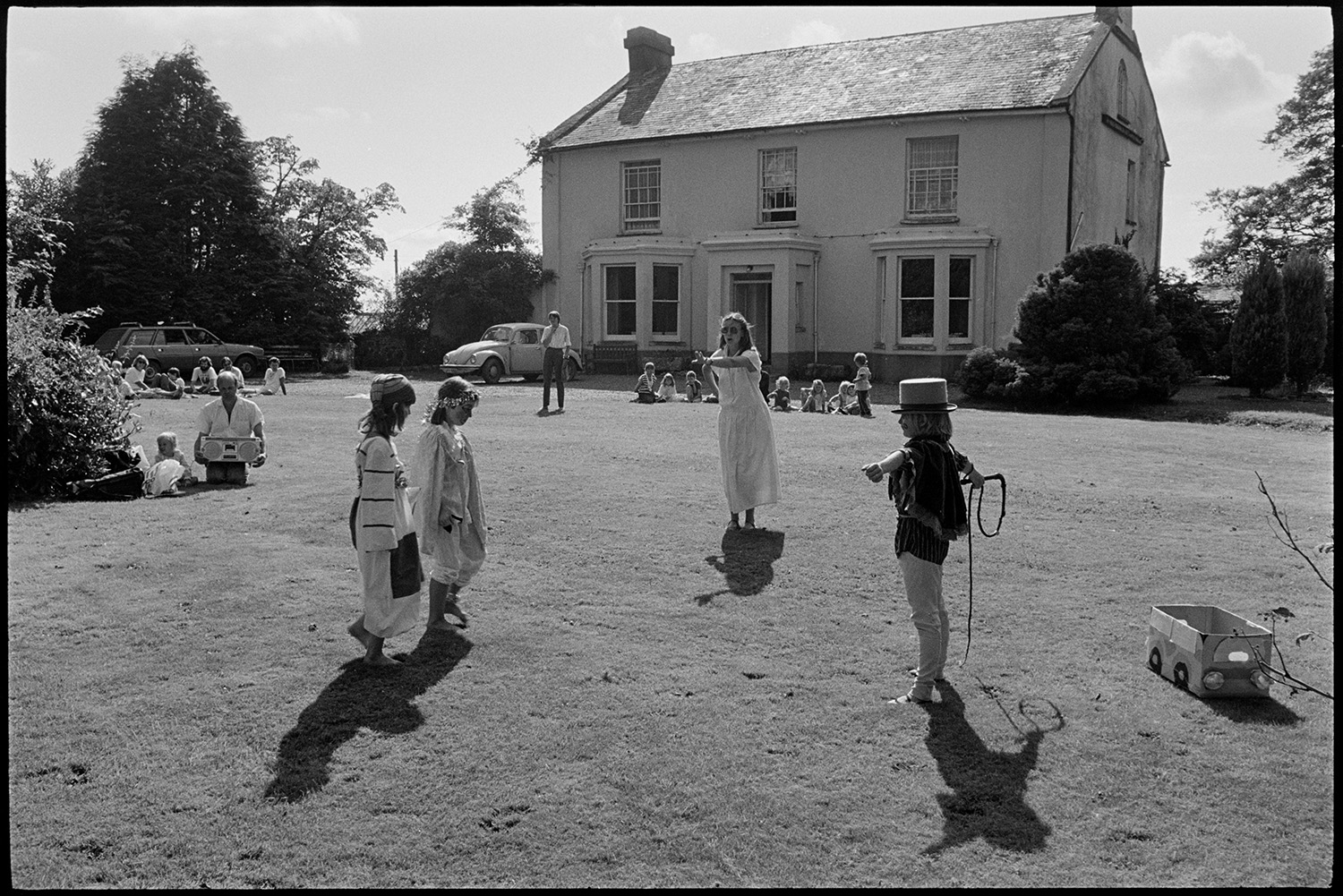 Children's ballet class dance performance on lawn of country house. 
[A woman teaching a ballet class to children on the lawn in front of Broadwoodkelly Rectory, which is visible in the background. The children are wearing costumes.]