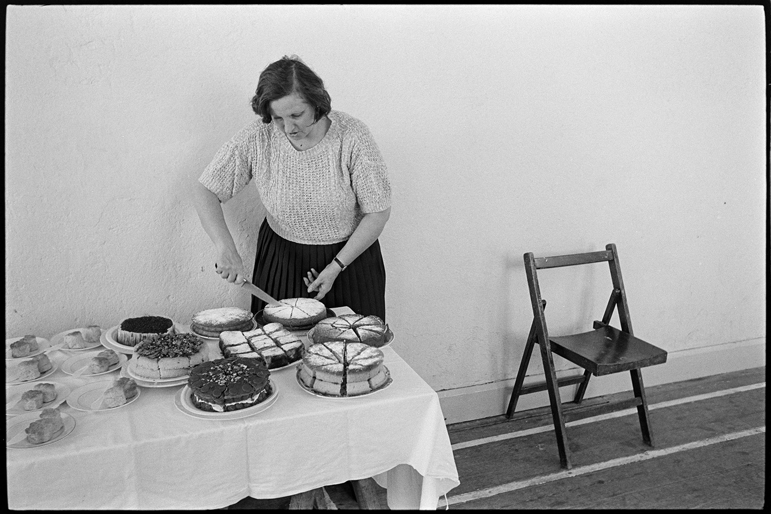 Children's ballet class dance tea in village hall being prepared, lots of cakes!! 
[A woman cutting up cakes for refreshments at a children's ballet class at Broadwoodkelly Village Hall.]