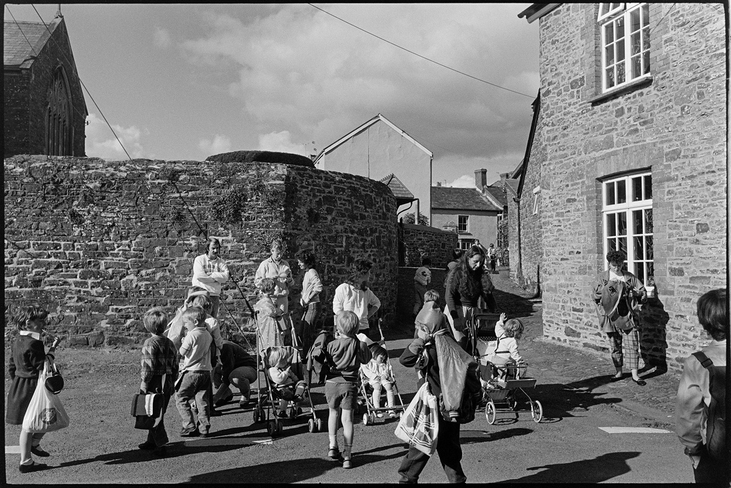 Street scenes, cottages, pub and chemist, mothers and children. 
[Parents, including mothers with prams, collecting their children from Chulmleigh Primary School.]