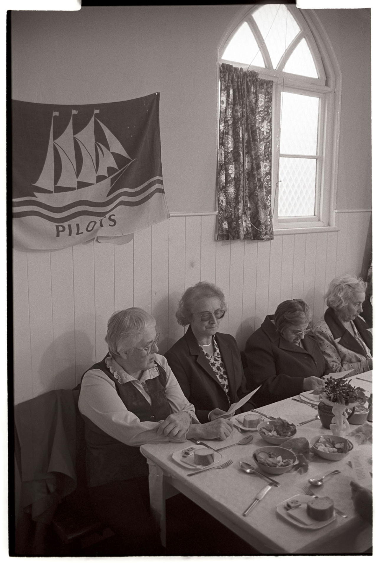 Congregational chapel Harvest supper, singing after meal. 
[Elaine Marsh, Minister and other women sat a table at the harvest supper at the Chulmleigh Congregational Chapel. They are singing a song before the supper.]