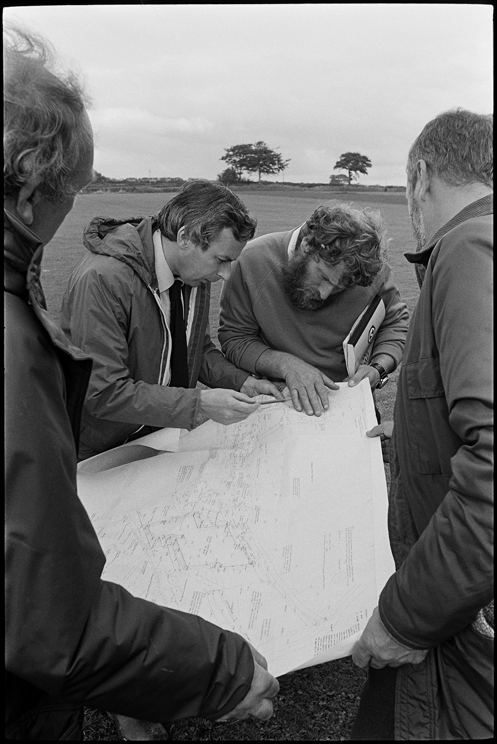 Planners, architects, teacher meet on site to discuss plans for new school.
[Planners, architects and teachers meeting in a field in Chulmleigh to discuss the site of the new school. They are looking at a large map or plan.]