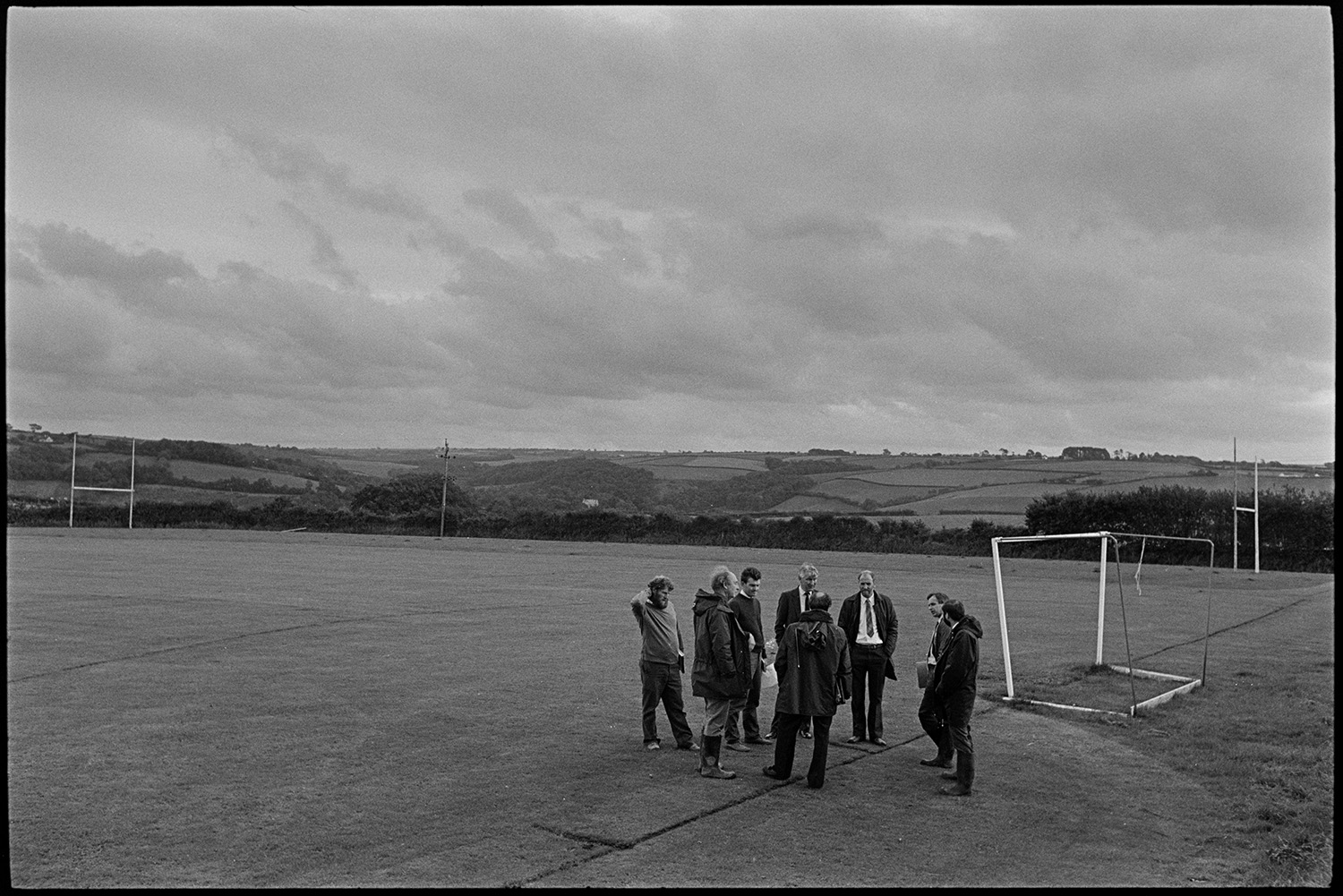 Planners, architects, teacher meet on site to discuss plans for new school.
[Planners, architects and teachers meeting in a field in Chulmleigh to discuss the site of the new school. They are standing in a sports field with rugby and football goal posts. Woodland and fields are visible in the background.]