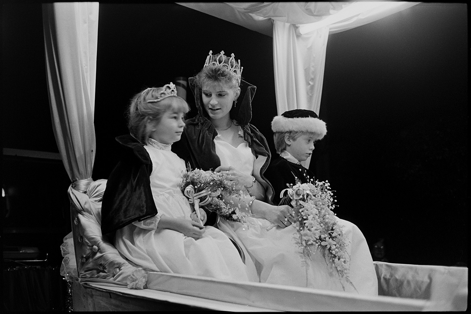 Carnival floats at night, Queen and attendants, fancy dress.
[The Dolton Carnival Queen and her two young attendants sitting on a float during the evening procession at Dolton Carnival.]