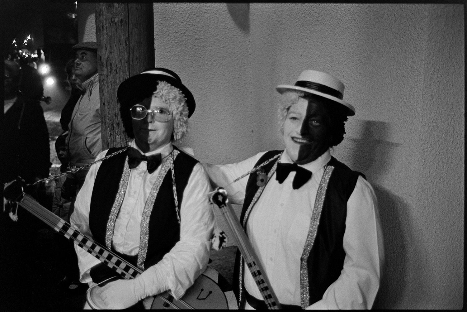 Carnival floats at night, queen and attendants, fancy dress.
[Two people dressed as black and white minstrels during the evening procession at Dolton Carnival. They are carrying banjos.]