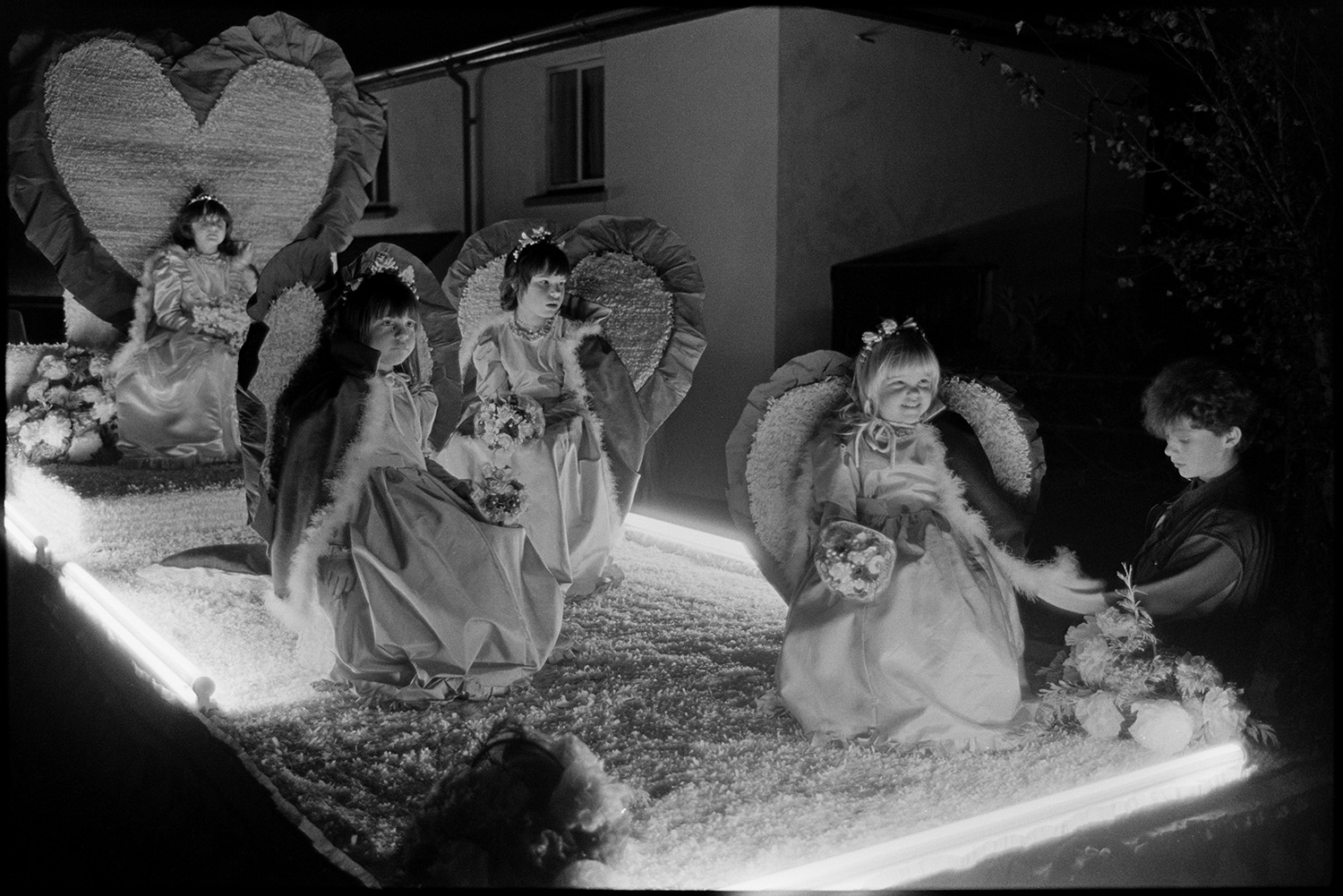 Carnival floats at night, queen and attendants, fancy dress, with burning torches.
[A carnival float during the evening procession at Dolton Carnival. Four girls in fancy dress sitting on a float decorated with heart shapes and flowers.]