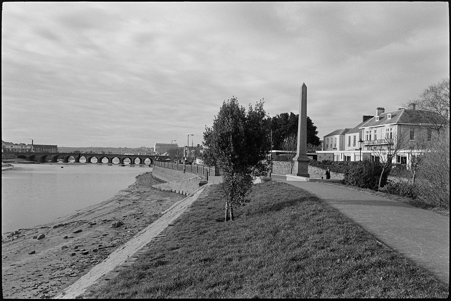 Towpath and bridge over Taw.
[View of the towpath beside the River Taw looking West towards the Long Bridge at Barnstaple, with an obelisk between the path and Taw Vale road.]