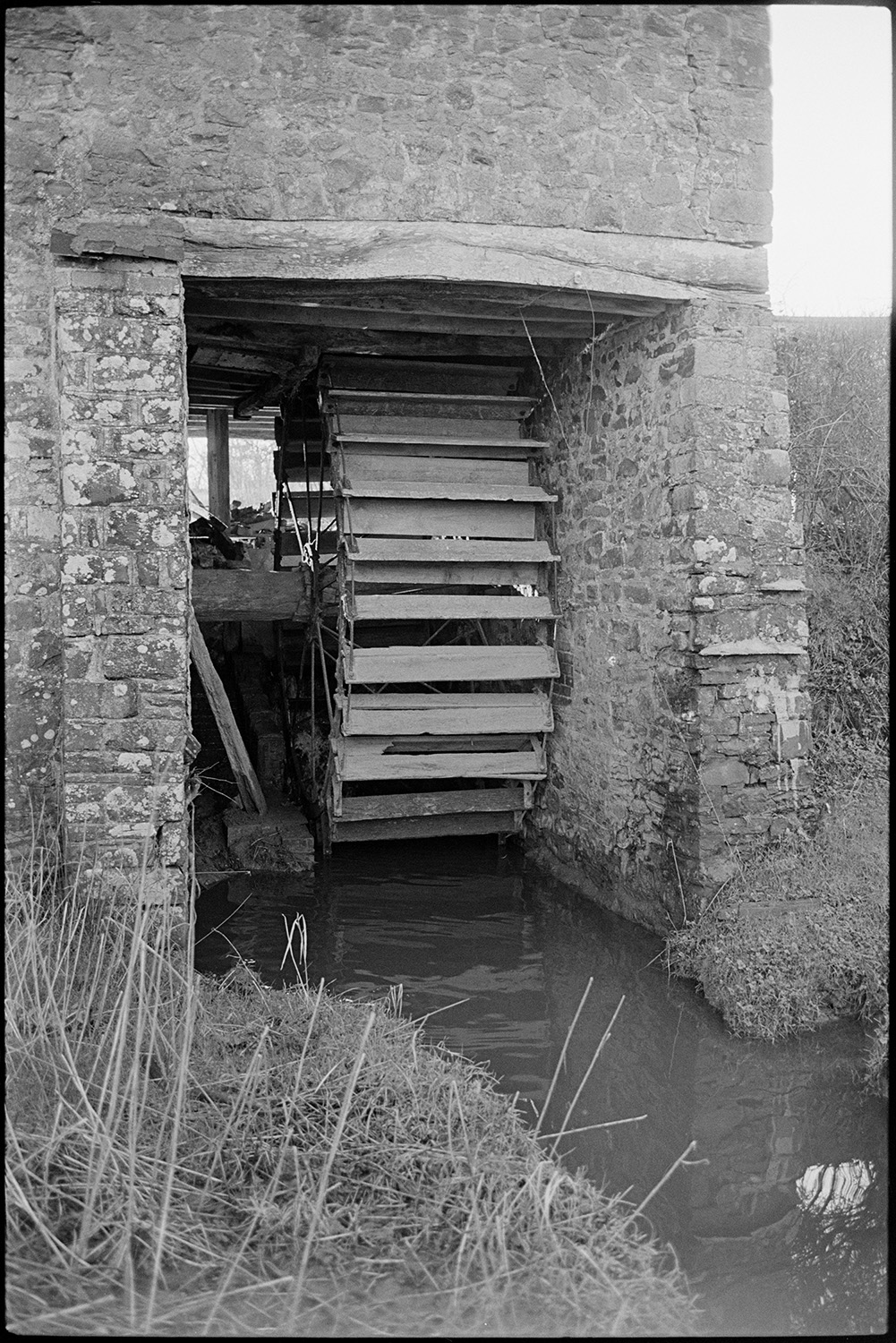 Views inside and outside of mill showing wheel and machinery and workshop. Stored nitches thatch.<br />
[The wooden water wheel at Rashleigh Mill, Bridge Reeve.]
