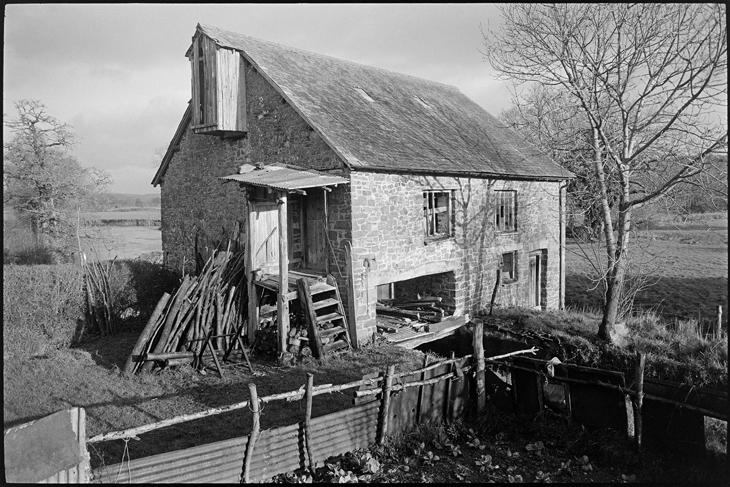 Views inside and outside of mill showing wheel and machinery and workshop. Stored nitches thatch.<br />
[Exterior view of Rashleigh Mill, Bridge Reeve, with a wood pile leaning against the end wall and a vegetable garden in front of the Mill. A set of wooden steps also leads up to the first floor of the mill.]
