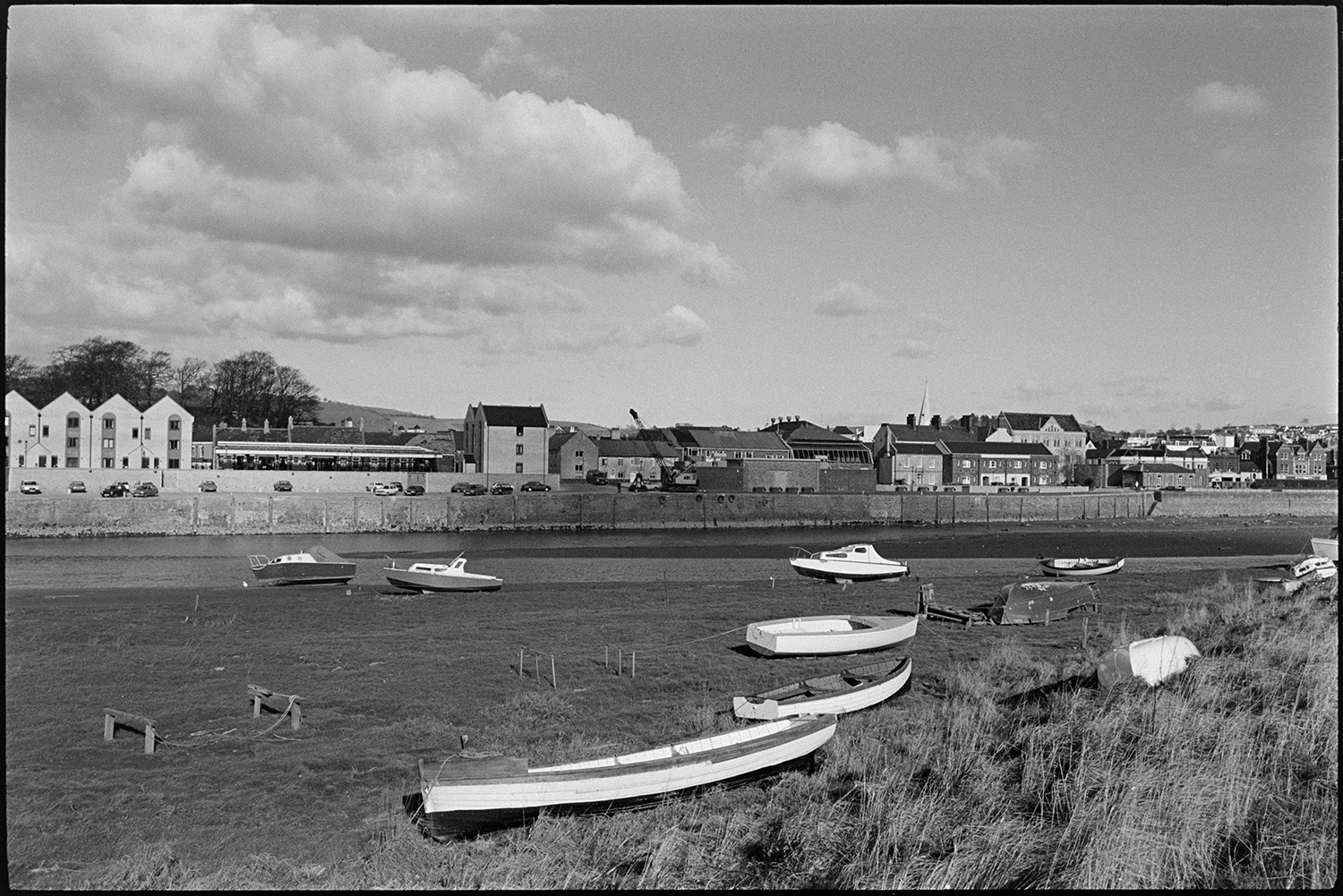 Barges and small boats on river bridge in background.
[Small boats and motor launches on the mud banks of the River Taw, with the buildings of Barnstaple on the other side of the river.]