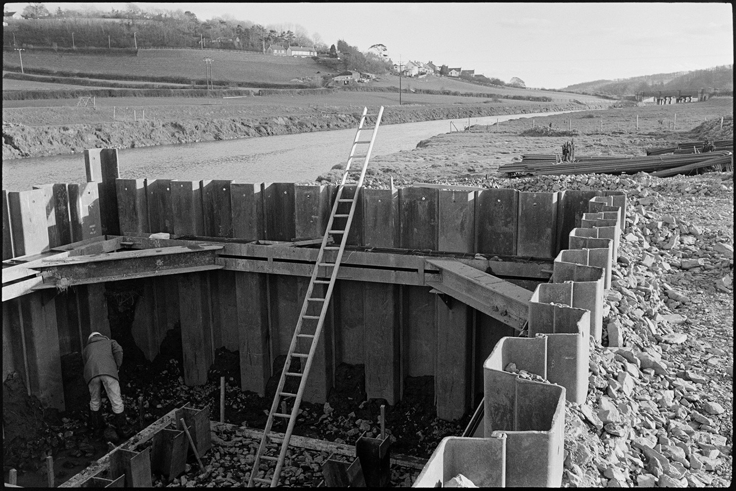 Engineers working on new river bridge for motorway link road.
[A man working on the bank of the River Taw near Barnstaple, inside the construction of the supports for a bridge being built across the river.]