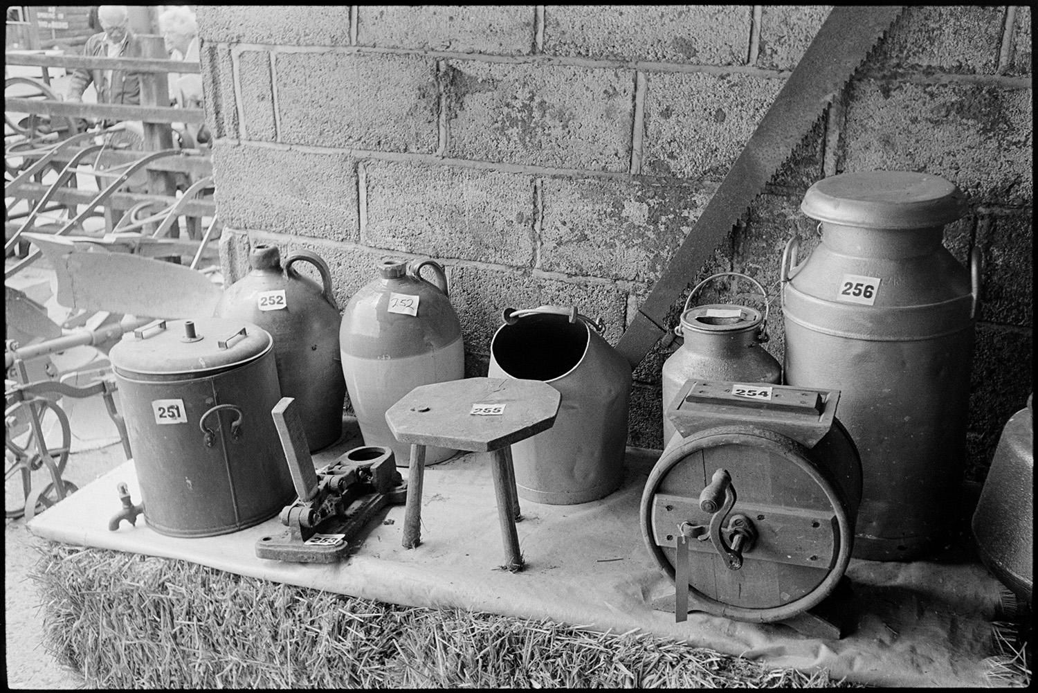 Sale of agricultural museum collection, signs, implements, machinery on display. Woodpile.
[Jugs, milk churns, stool and hand operated mixer being sold from the Ashley Collection at Hollocombe. The items are displayed on top of a hay bale.]