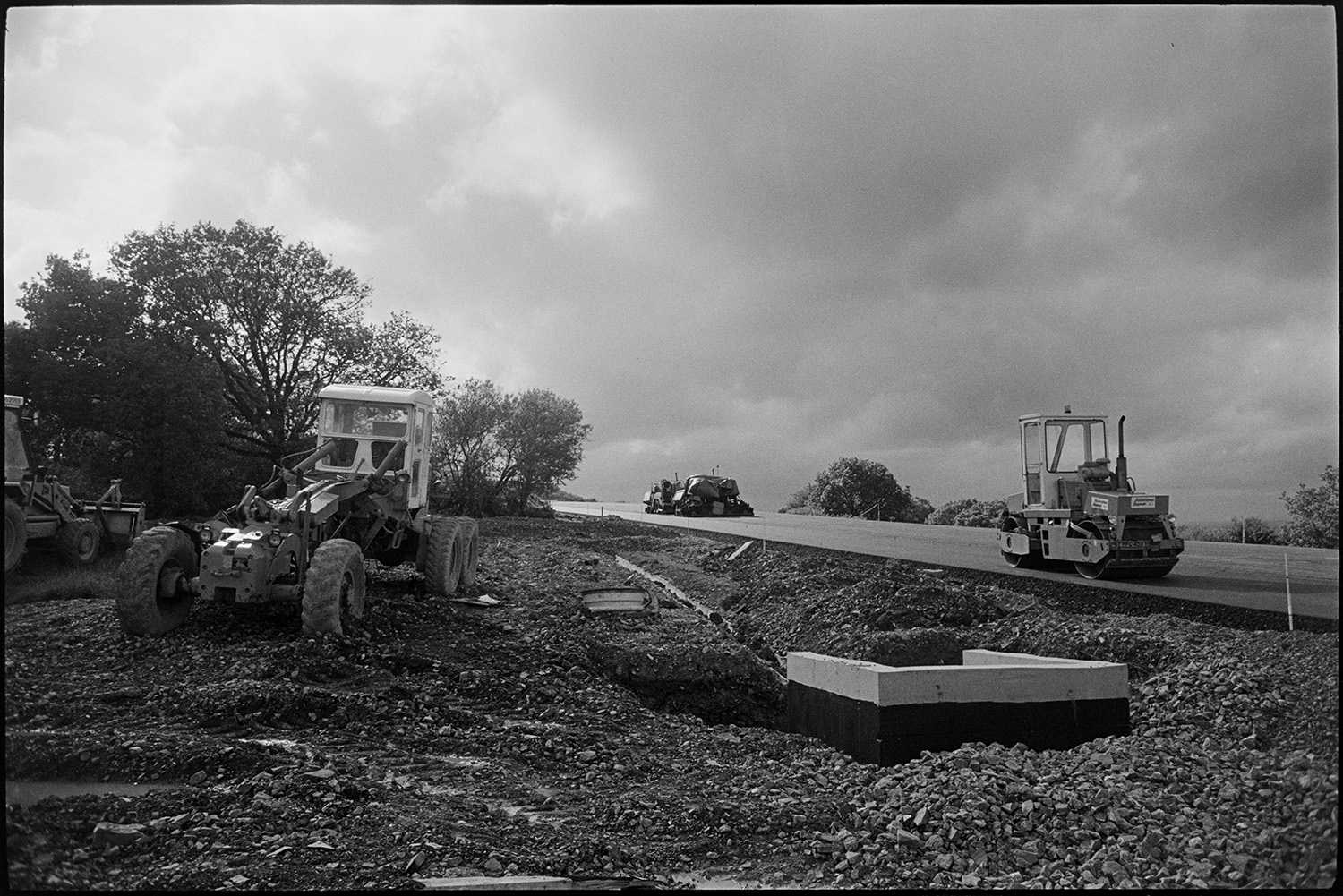 Machinery on new motorway link road shortly before it opened. Diesel roller and earth mover.
[A diesel roller and earth mover working on the North Devon link road near Rackenford shortly before it opened. A stormy sky is visible in the background.]