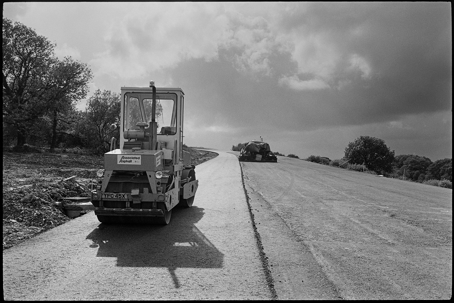 Machinery on new motorway link road shortly before it opened. Diesel roller and earth mover.
[A diesel roller working on the North Devon link road near Rackenford shortly before it opened. A stormy sky is visible in the background.]