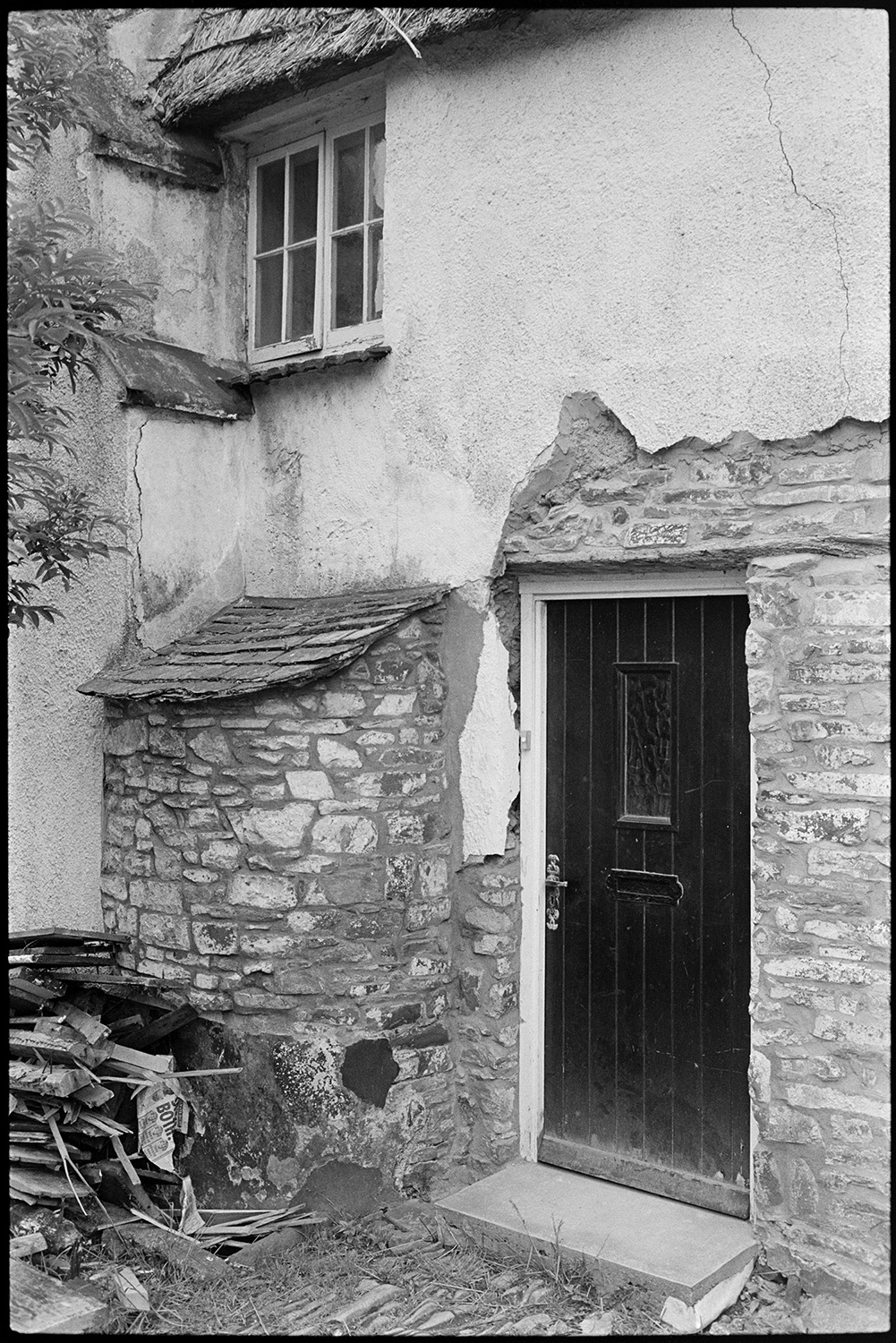 Back door of cottage with old bread oven, being renovated and ruined, see RAV/01/1603/17 for earlier image.
[The back door of a thatched cottage at Beaford during renovation. There is stonework being repointed on the exterior of a bread oven and around the door.]