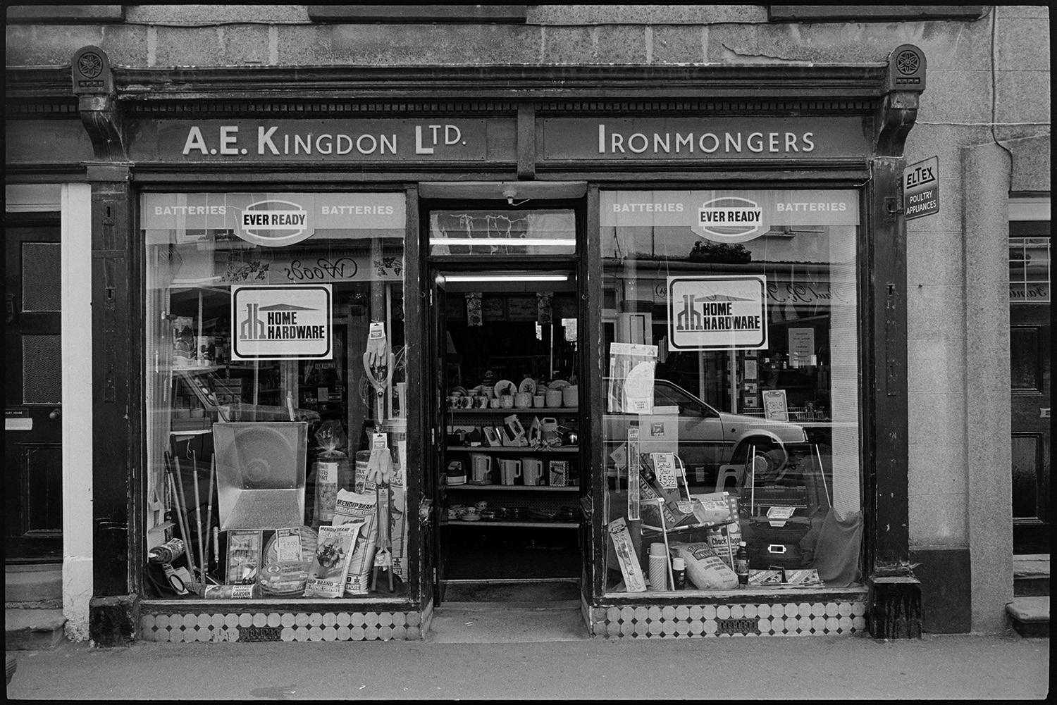 Front of ironmongers shop.<br />
[View of the shop front of A.E. Kingdon Ltd ironmongers shop in Fore Street, Chulmleigh with open door and window displays of goods including garden chairs, gardening tools, kettles and china.]