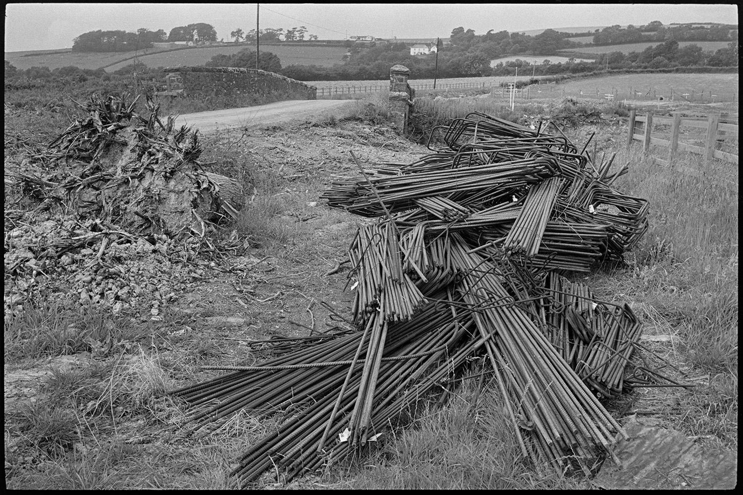 Surveying new link road, mechanical digger, piles of steel for reinforcement. <br />
[Steel rods for reinforcement piled on the roadside next to the site of the new Devon Link Road near South Molton. A stone bridge can be seen in the background.]