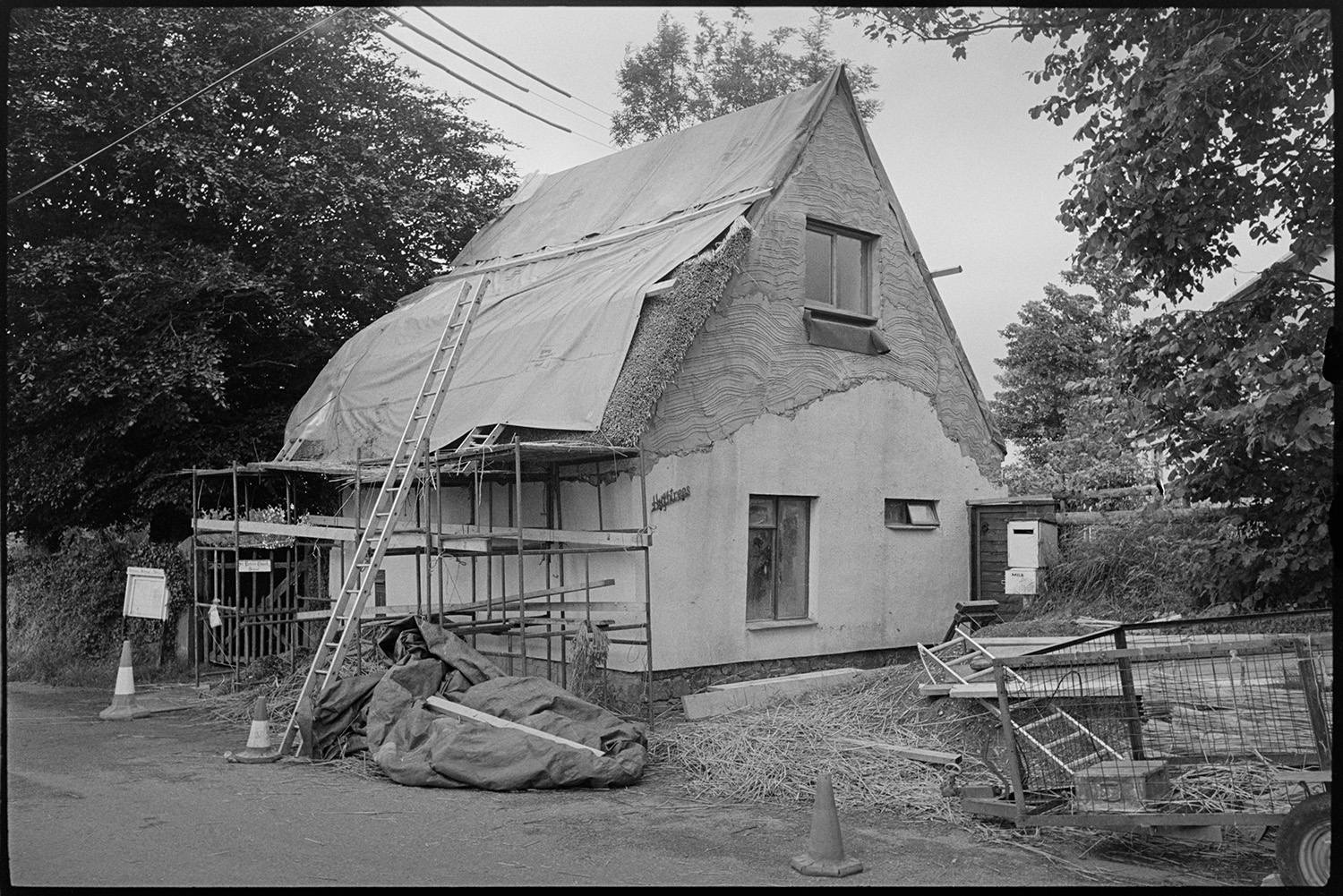 Former thatched stable being converted to housing, see earlier pictures. <br />
[A thatched stable being converted to a residence at Church Gate, Dowland. The thatched roof is covered and scaffolding and a ladder are erected against one wall.] 