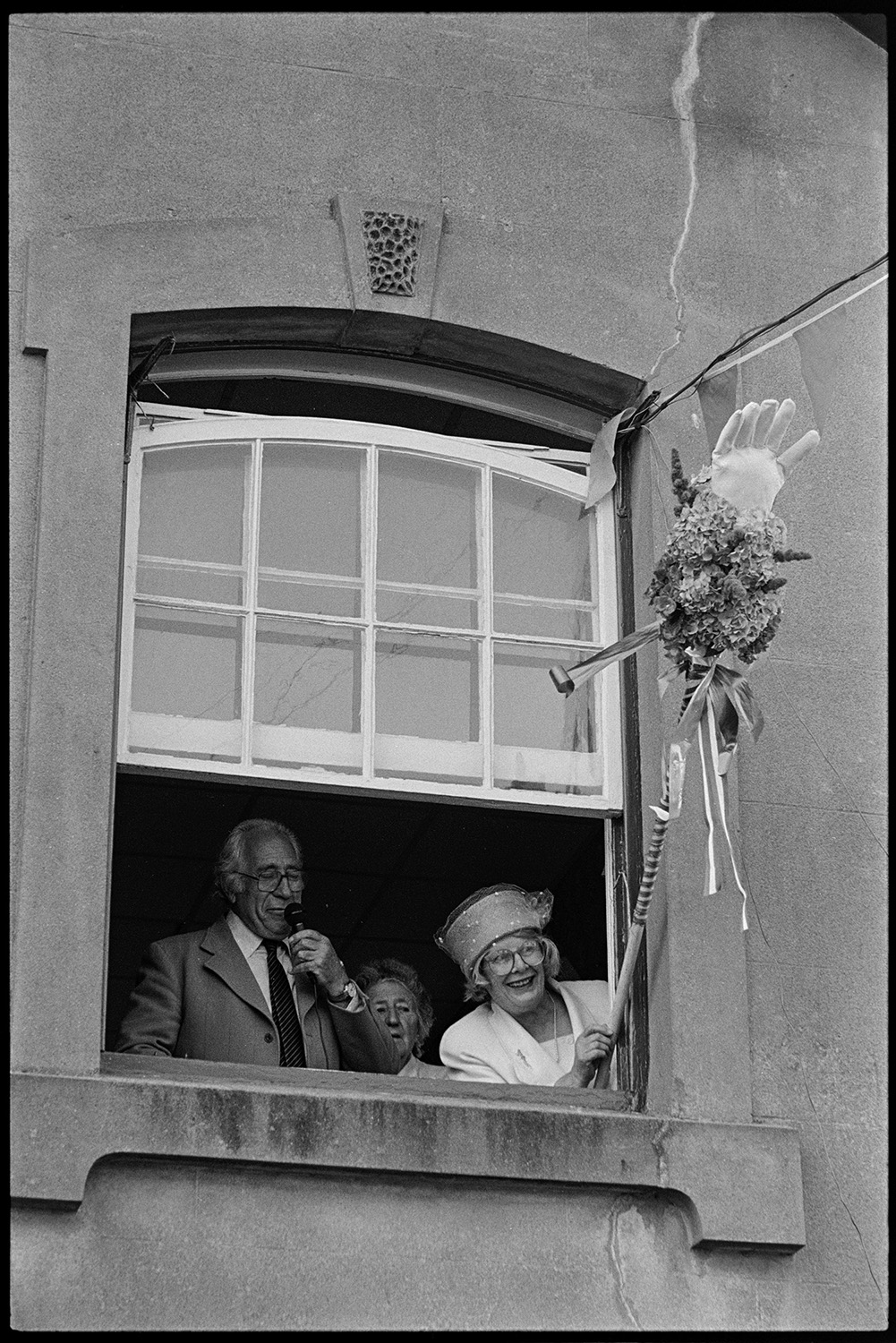 Fair Queen, woman opening fair, crowd of children at money scramble. 
[Evelyn Prince and Joe Fullbrook opening Chulmleigh Fair from a window in the town hall. Evelyn Prince is waving the ceremonial glove  from the window.]