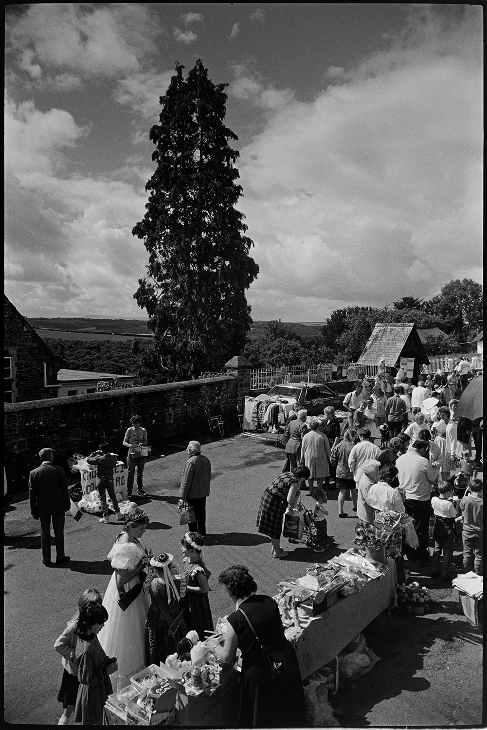 Fair, money scramble, races stalls, fancy dress. 
[Visitors to Chulmleigh Fair looking at stalls with clothes and bric-a-brac. The Fair Queen is looking at a stall in the foreground.]