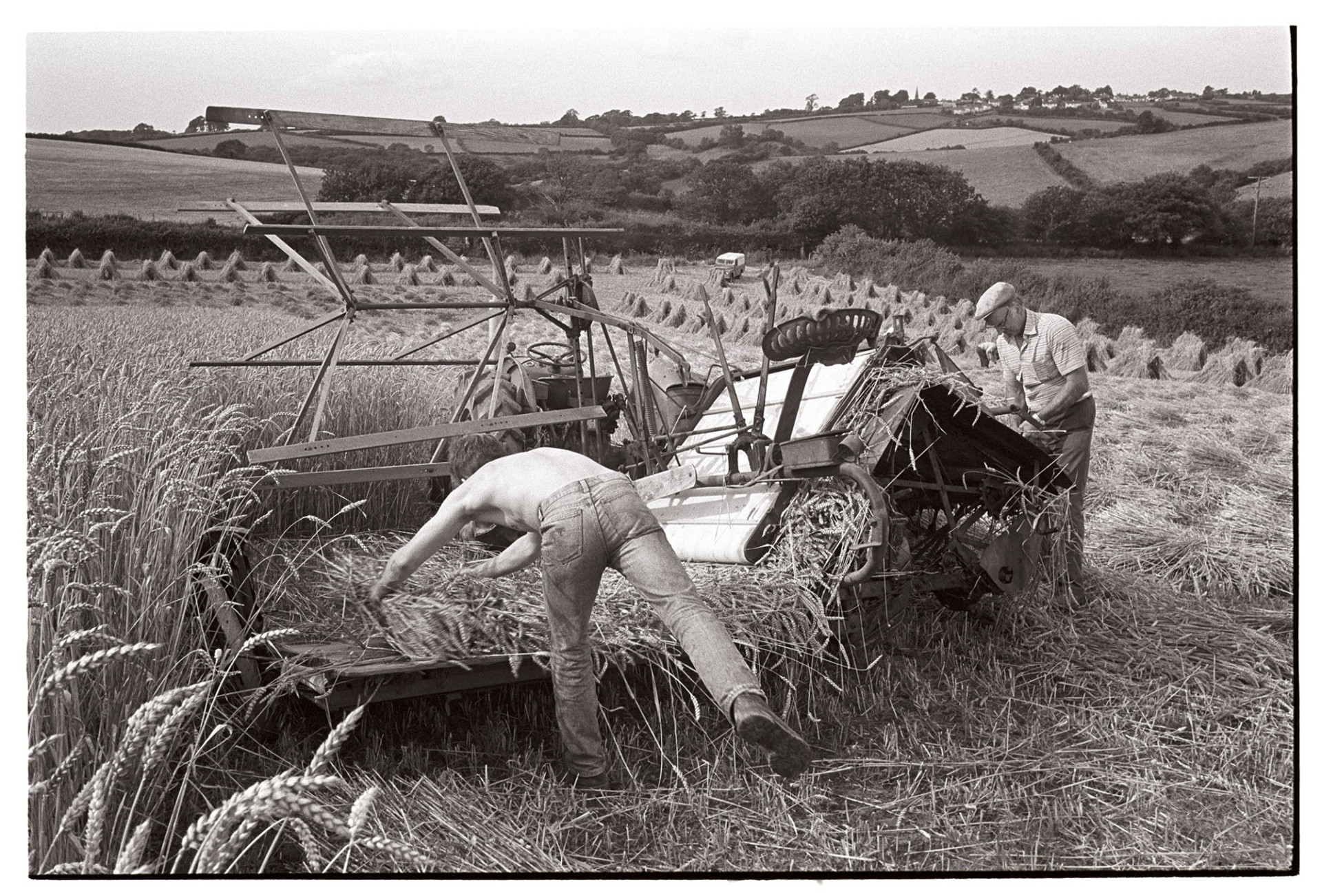 Farmers unblocking reap and binder which had jammed. 
[Two men fixing a reap and binder which had jammed while harvesting corn in a field at Spittle, Chulmleigh. Stooks of corn can be seen in the background.]