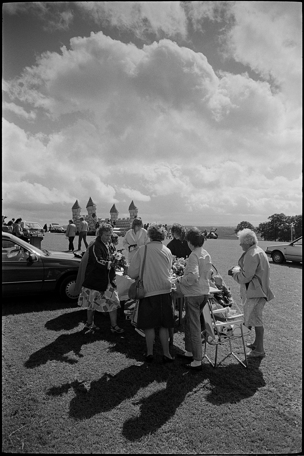 Sports Day, sheep dog trials, races, stalls, football. 
[A group of women looking at a flower stall at a sports day and car boot sale in Chulmleigh playing field. Parked cars and a bouncy castle can be seen in the background.]