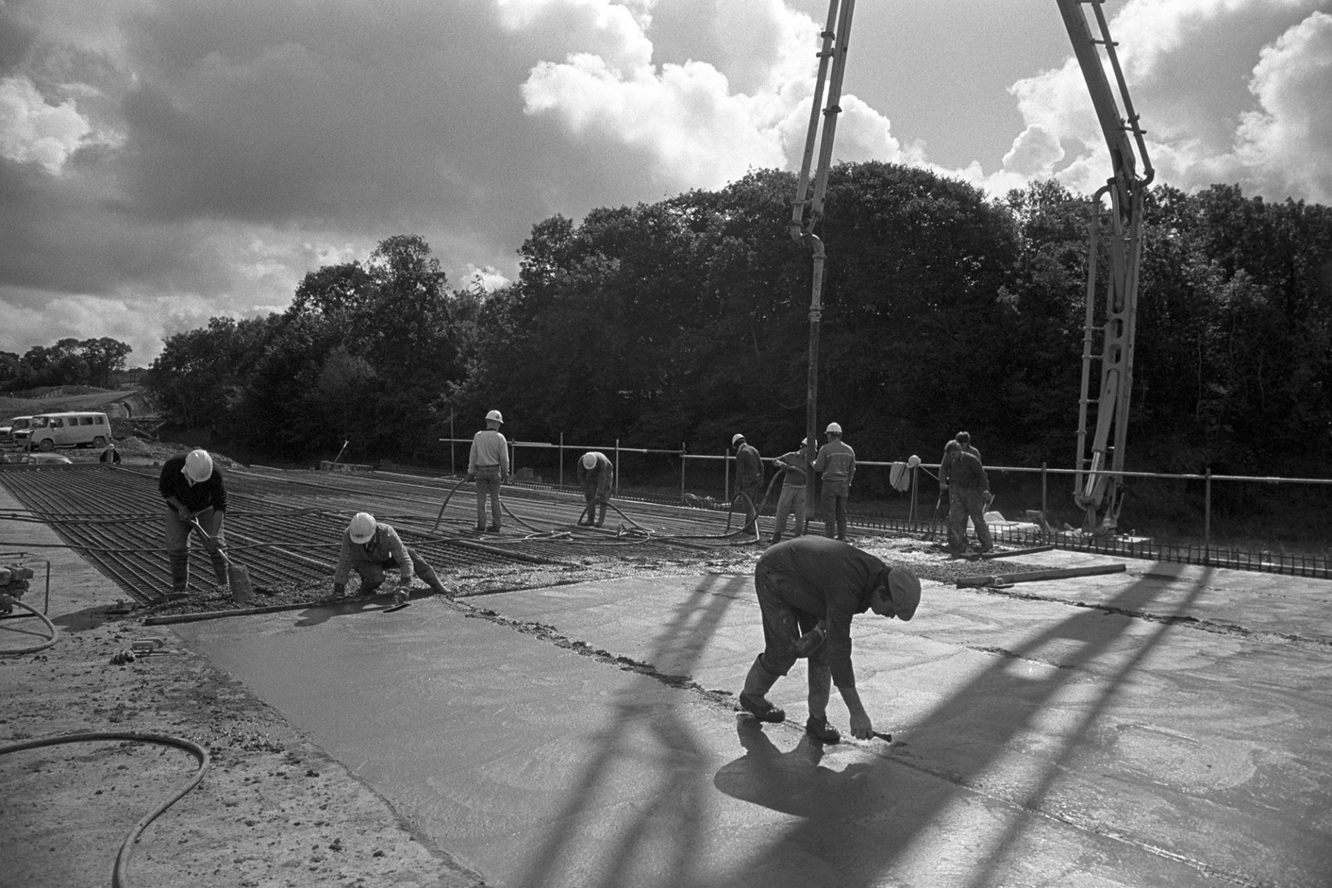 Men building new link road laying cement delivered by crane, sun and cloud. 
[Men laying cement on the new North Devon Link road or A361 foundations near South Molton. The cement is being pumped in by a crane.]