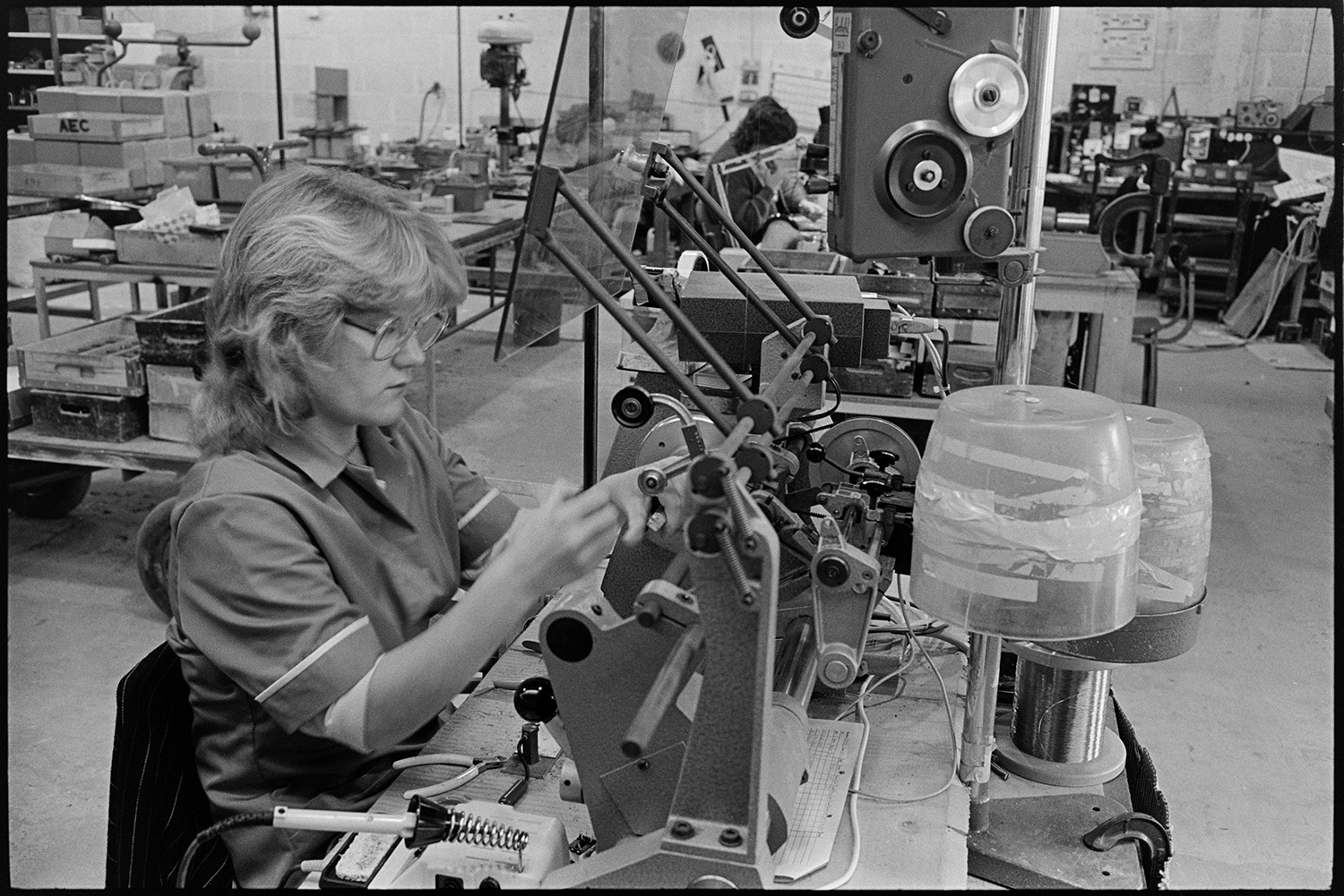 Inside transformer factory men and women making, designing transformers, computer. 
[A woman making transformers at Apex Transformers at Pathfields Business Park in South Molton. Other machinery can be seen in the factory in the background.