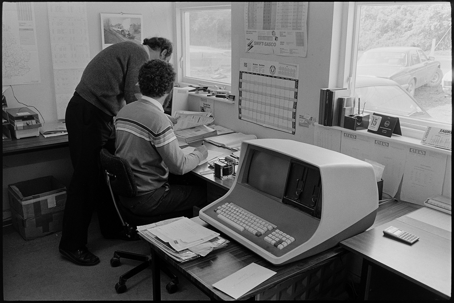 Directors of transformer factory in office working and using computer. 
[Two men looking at papers on a desk in the office at Apex Transformers at Pathfields Business Park, South Molton. A computer is on the desk beside them.]